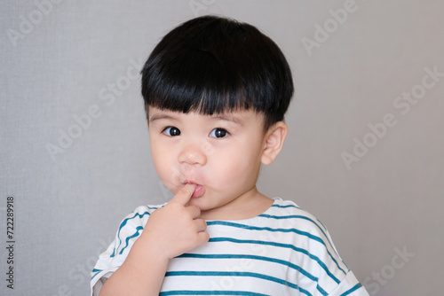 Portrait of funny baby toddler sucking finger, asian baby making funny face isolated on gray background