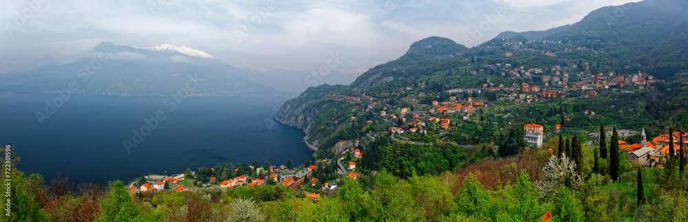Obraz premium A panoramic view from Vezio Castle on the mountainside overlooking beautiful Lake Como with villages on lakeside hills and snow capped alpine mountains in background on a cloudy day, in Varenna, Italy