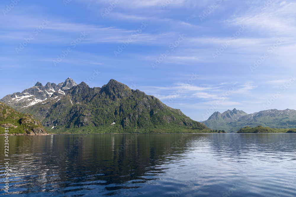 Calm waters mirror the dramatic mountain scenery of Lofoten, Norway, bathed in the light of a bright summer day