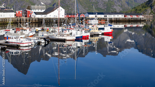 In Hamnoy, the stillness of the fjord creates perfect reflections of fishing boats and colorful waterfront buildings against a mountain backdrop. Lofoten Island, Norway