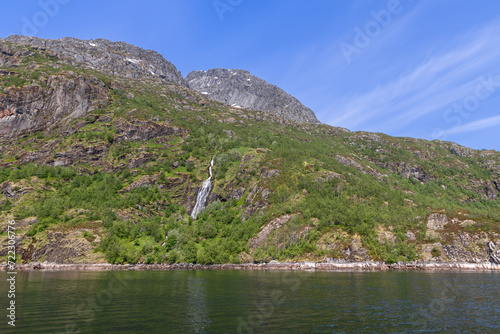 A cascading waterfall tumbles down a rocky mountainside into a fjord in Trollfjorden, Norway photo