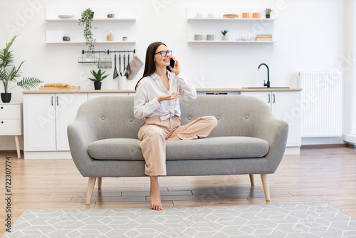 Beautiful woman relaxing on sofa at home and using modern smartphone for talking with family. Caucasian brunette using modern devices enjoying break from work for business negotiations on weekend.