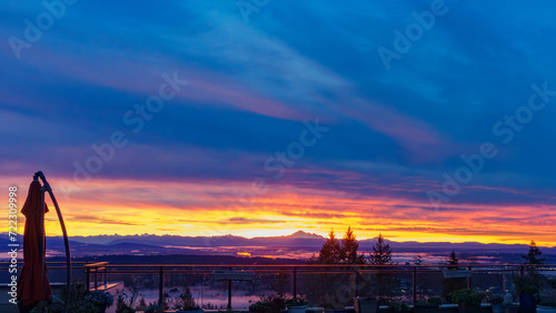 Vivid sunrise over Fraser Valley, BC, with backdrop of mountains in silhouette, as viewed from a Burnaby Mountain patio.