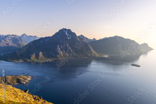 A tranquil dusk with the midnight sun at Offersoykammen, casting golden hues over the Nappstraumen strait surrounded by the dramatic Lofoten mountains