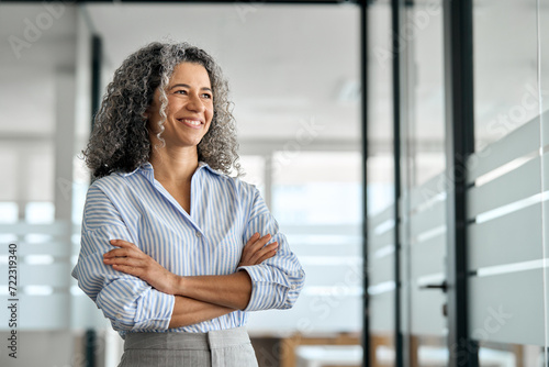 Smiling happy confident old mature professional business woman corporate leader, senior middle aged female executive, lady bank manager standing in office hallway arms crossed looking away, portrait. photo