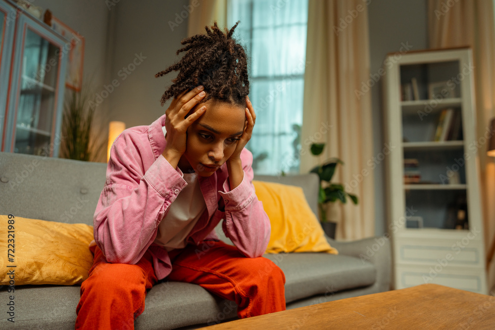 Portrait of tired lonely African American woman having headache, depression, sitting on sofa at home Portrait of tired lonely African American woman having headache, depression, sitting on sofa at home