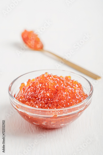 Natural salty salmon red caviar or organic fish roe served in glass bowl on white wooden table with spoon of golden colour used as spread or ingredient for breakfast full of vitamins, protein and fat