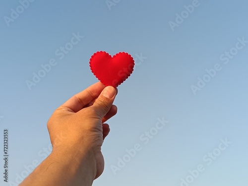 Red heart with hand under blue sky and sun light background, love and valentines day concept.