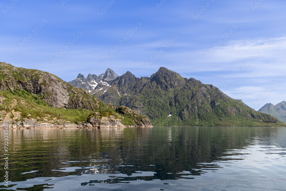 The mirror-like waters of Trollfjorden reflect the grandeur of the Lofoten peaks, with snow patches accenting the mountain's rugged green slopes