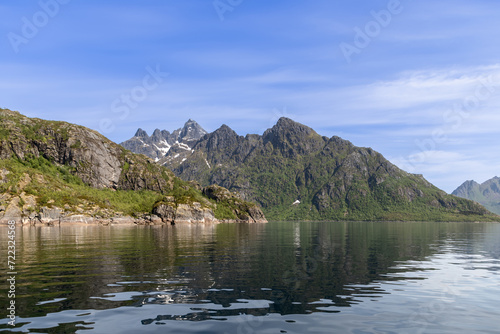 The mirror-like waters of Trollfjorden reflect the grandeur of the Lofoten peaks, with snow patches accenting the mountain's rugged green slopes