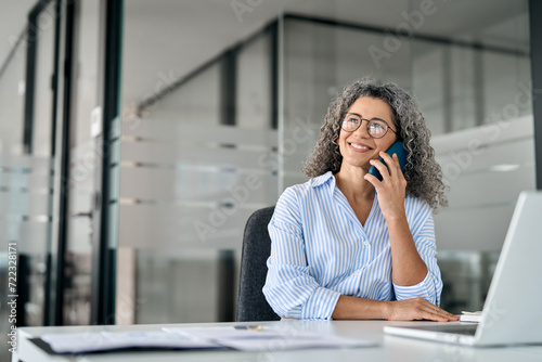 Happy older middle aged business woman speaking on phone in office. Busy smiling mature professional lady manager making business call talking to customer on cellphone looking away at work. Copy space