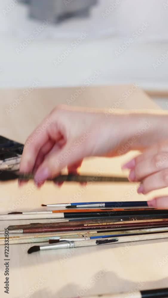 Vertical video. Art tools. Creative accessories. Closeup of woman painter hands choosing paintbrushes for drawing at artwork table studio workplace. Vertical video. Art tools. Creative accessories. Closeup of woman painter hands choosing paintbrushes for drawing at artwork table studio workplace.