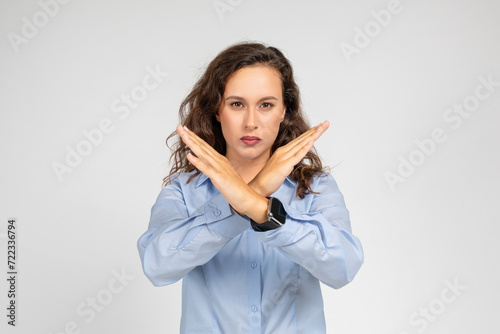 A determined young woman in a blue shirt makes an X sign with her arms photo