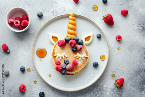 Top view of unicorn shape made from pancakes , decorated with berries and honey. On the simple plate.