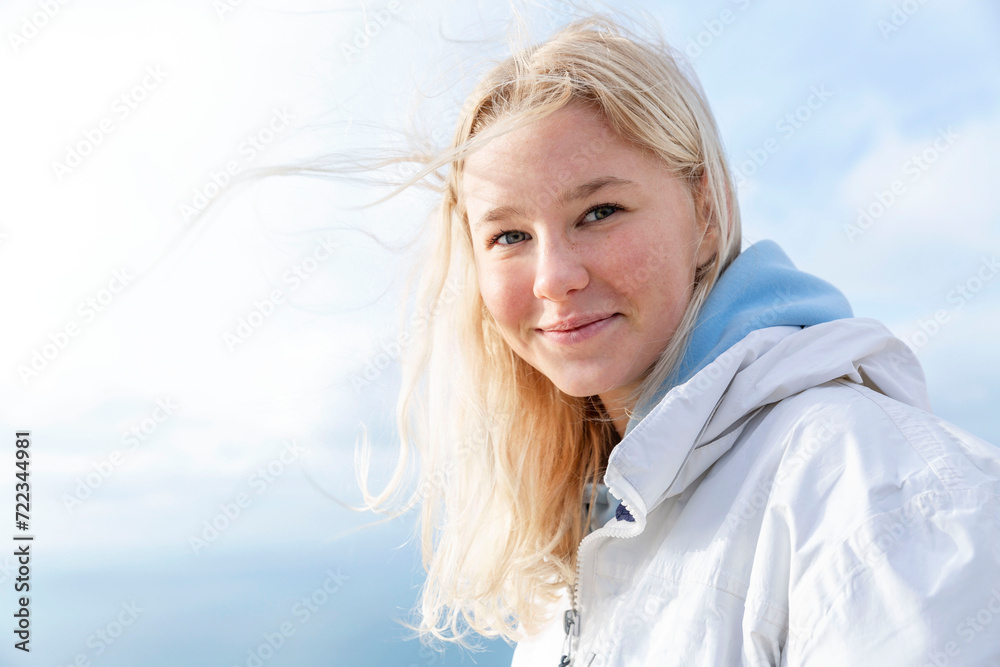 A young girl smiles against the blue sky on a sunny windy day. Cute blonde with flowing hair. Freedom and happiness. Close-up. A young girl smiles against the blue sky on a sunny windy day. Cute blonde with flowing hair. Freedom and happiness. Close-up.