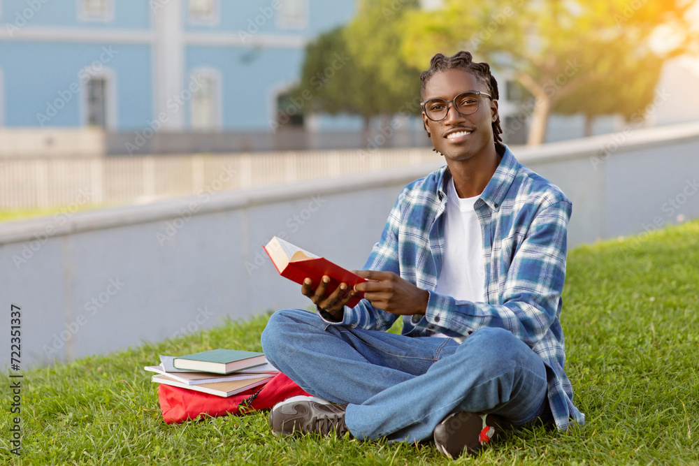 Obraz premium Happy African American student guy casually reads book outdoor