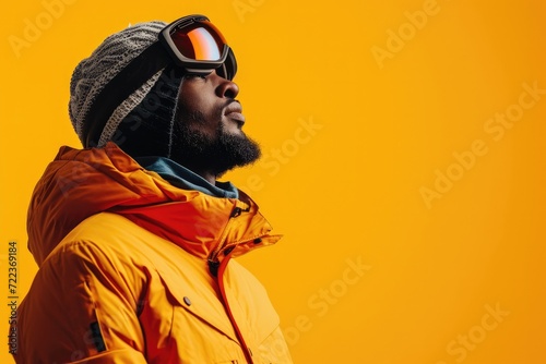 A man in an orange sports jacket and glasses for skiing, snowboarding. Studio photo of a skier, snowboarder on an orange background, close-up view © Diana Galieva