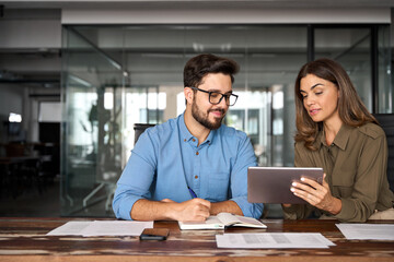 Professional happy manager showing work plan using tab helping employee. Busy colleagues working with digital tablet talking in office. Smiling professional partners having conversation at meeting.