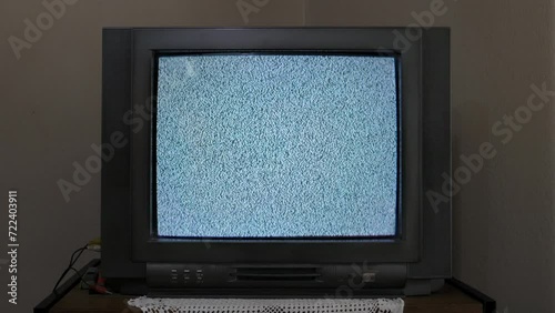 An old CRT TV sitting on a shelf, with no signal, displays static white noise photo