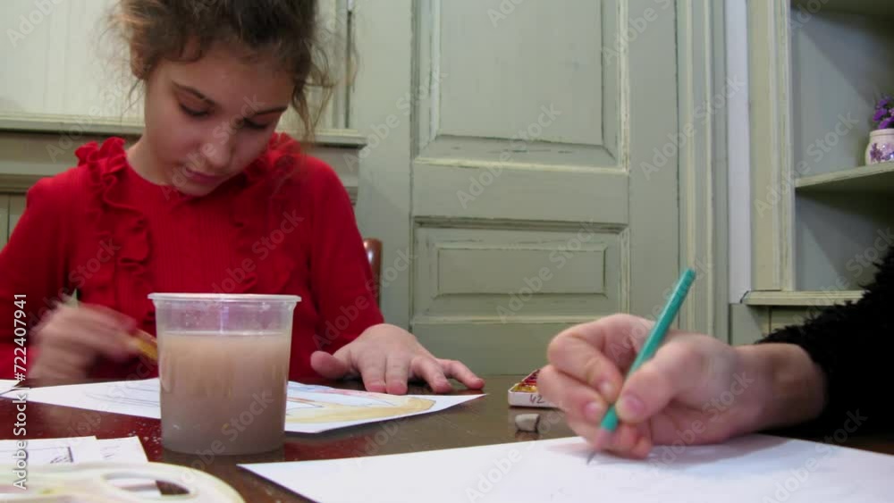 Young girl draws by brush and paints on paper at table in class room. Timelapse