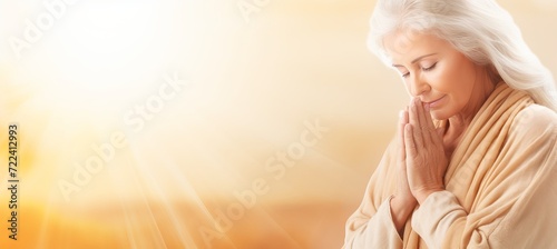 Devout senior woman praying at church, hands raised in worship towards divine light, space for text