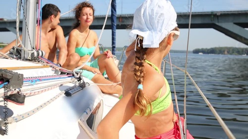 Side of girl sitting on border of swimming yacht near woman and man on bow photo