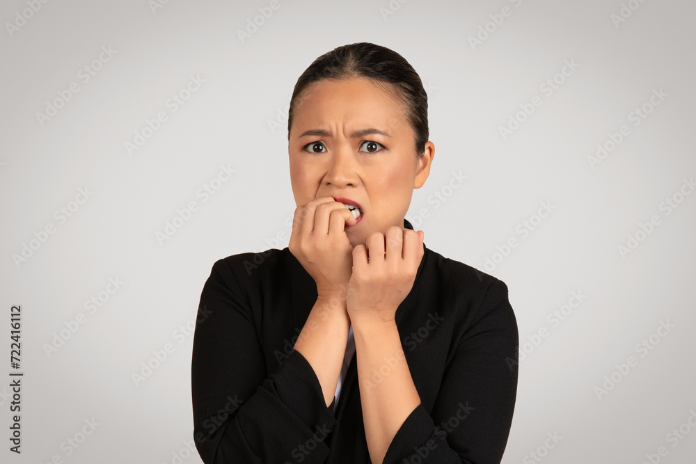 Anxious Asian businesswoman in a black blazer with a look of fear, nervously biting her nails Anxious Asian businesswoman in a black blazer with a look of fear, nervously biting her nails