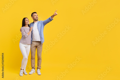 Look There. Happy caucasian couple standing and pointing aside at copy space