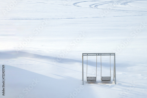 Panoramic view of snowy desert with snowmobile tracks. Lonely snow-covered swings in the foreground. Copy space. photo