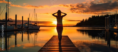 young woman doing yoga on a dock at sunset back view photo