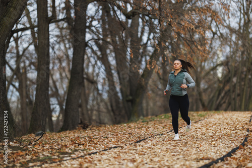 Valokuva Woman Running Down a Leaf Covered Trail in Autumn Forest