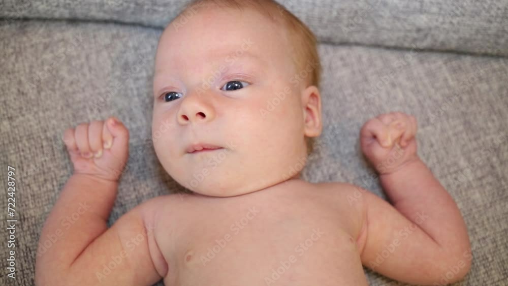 Baby boy clenched his hands into fists and lies on a gray couch Baby boy clenched his hands into fists and lies on a gray couch