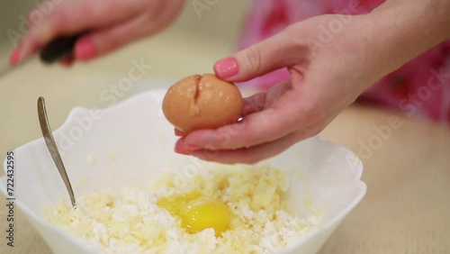 Woman is braking eggs by knife and put it to the quark with cheese in bowl photo