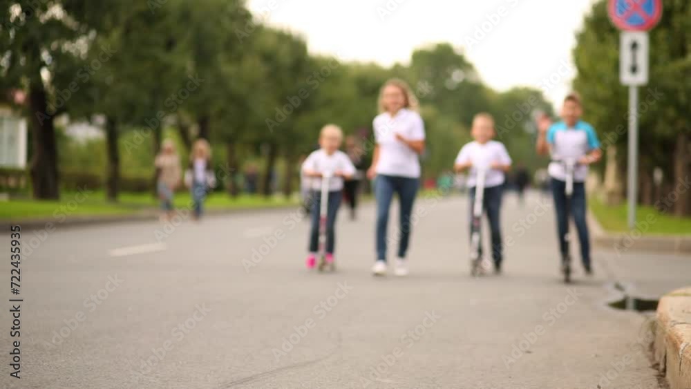 Woman runs next to three children on scooters on the street Woman runs next to three children on scooters on the street