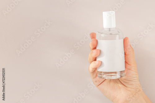 female hand holding a bottle of perfume with a beige label on a beige background  space for your text.
