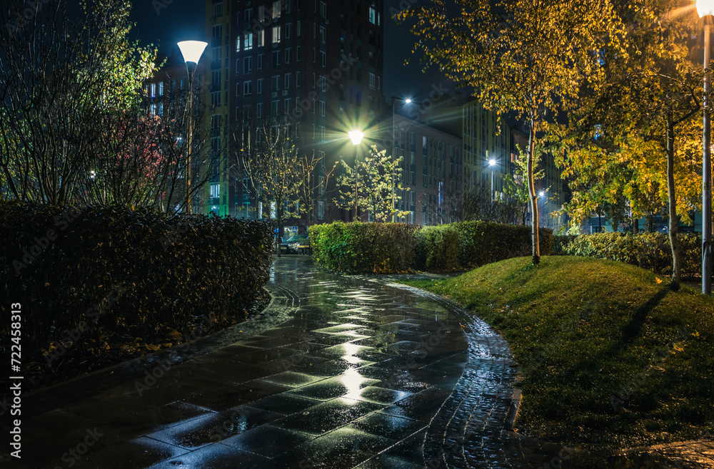 Obraz premium Night park paths and colored houses on a rainy autumn night. Night paths, benches, lanterns in a beautiful residential complex. Night autumn park with lanterns, benches, yellow leaves. Kyiv. Ukraine