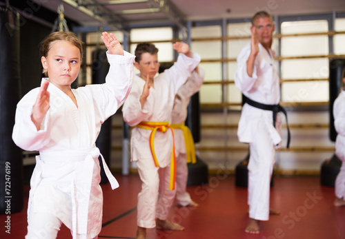 Female karate fighter in white kimono, combat stance. Children in a pair practice karate