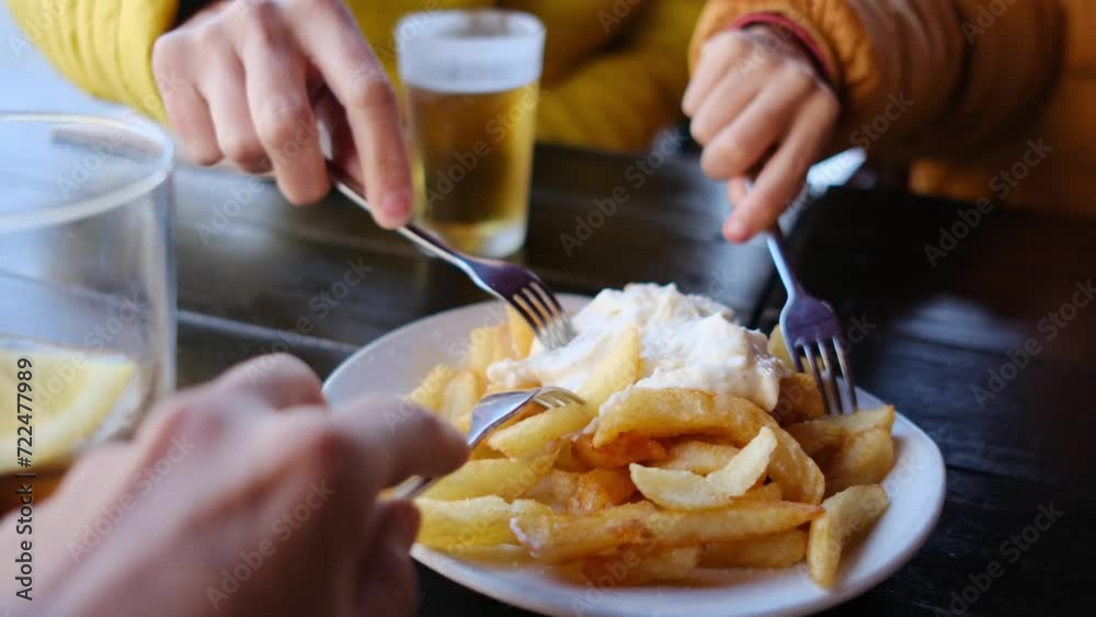 Family eating Spanish tapas on a terrace of a restaurant in Barcelona, patatas bravas, pescado frito and other typical tapas. Subjective point of view, hand and food, action.
