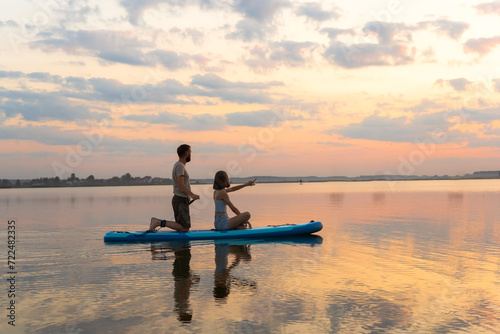 Happy couple paddle boarding at lake during sunset together. Concept of active family tourism and supping. aesthetically wide shot.