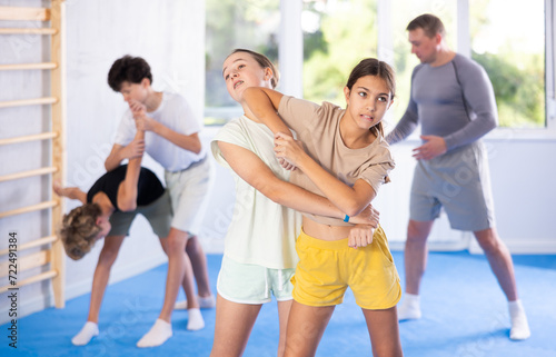 Two preteen girls train in pairs at self-defense lesson under guidance of trainer in the gym
