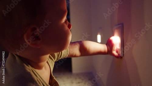Close-up of a baby touching a nightlight on the wall, the soft light casting a warm glow on their curious face in a dim room. photo