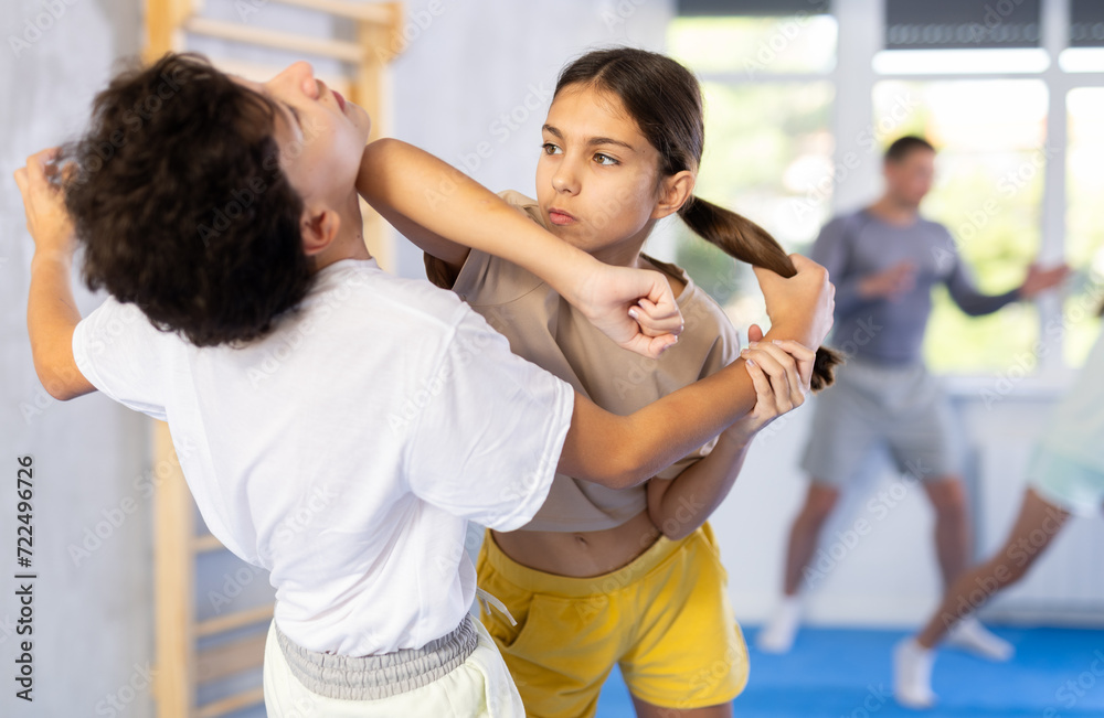 Fototapeta premium Boy and girl paired up and practice to aim stroke to neutralize opponent and repulse attack. Class self-defense training in presence of experienced instructor