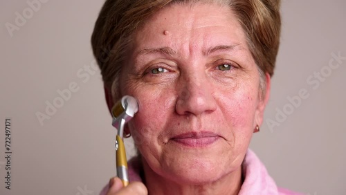 portrait head shoot of beautiful elder woman using derma roller with needles for facial rejuvenation, face anti aging wrinkle procedures at home. smiling female granny photo