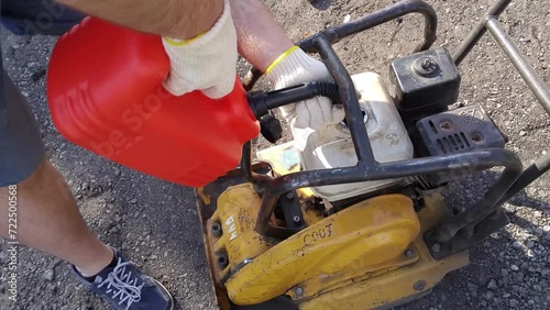 Hands of man holding red oilcan and refueling plate compactor close up