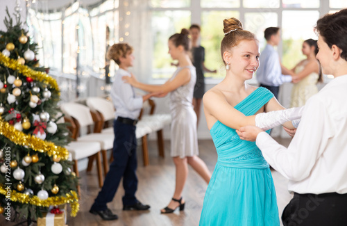 Smiling elegant teenage girl dancing slow waltz as couple with classmate during festive Christmas party at college