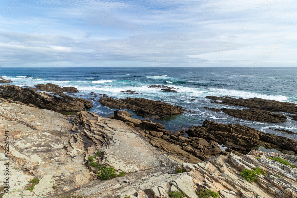 A beautiful rocky shoreline with waves crashing under a partly cloudy sky, exuding serene and natural beauty