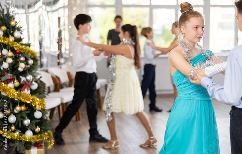 Positive teen boy and girl are dancing classic version of waltz in couple during lesson at studio in New Year atmosphere. Leisure activities and physical activity for positive children.