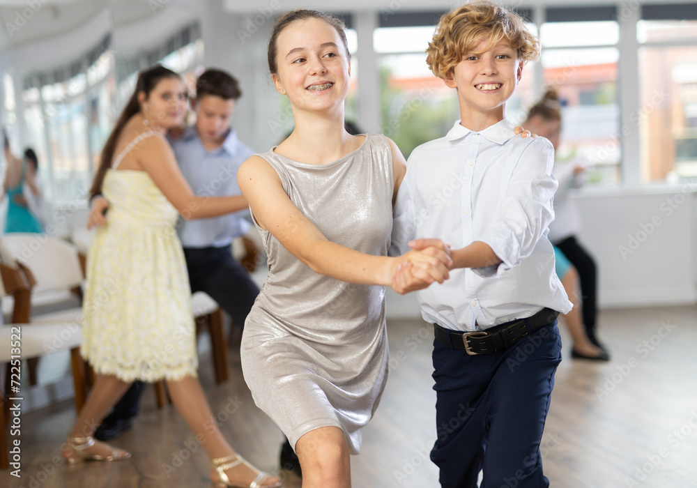 Fototapeta premium Positive teen boy and girl are dancing contemporary modern discofox in couple during lesson at studio. Leisure activities and hobby for positive people.
