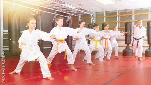 Group of preteen boys and girls doing karate kicks with male coach during karate class