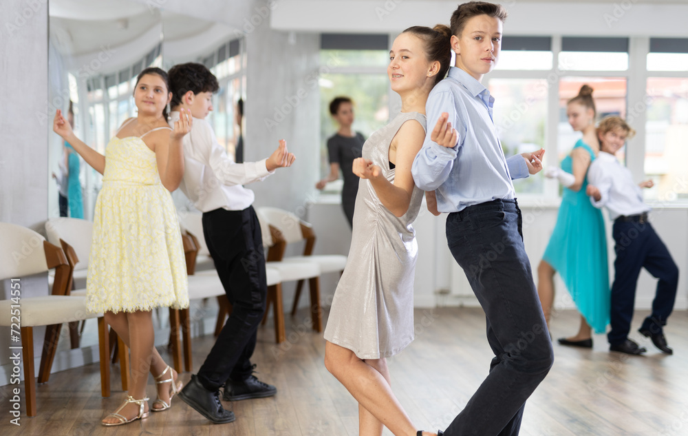 Group of positive teenagers, girls and boys, rehearsing jazz-style routine in dance studio. Partners standing back-to-back in pairs and snapping fingers..